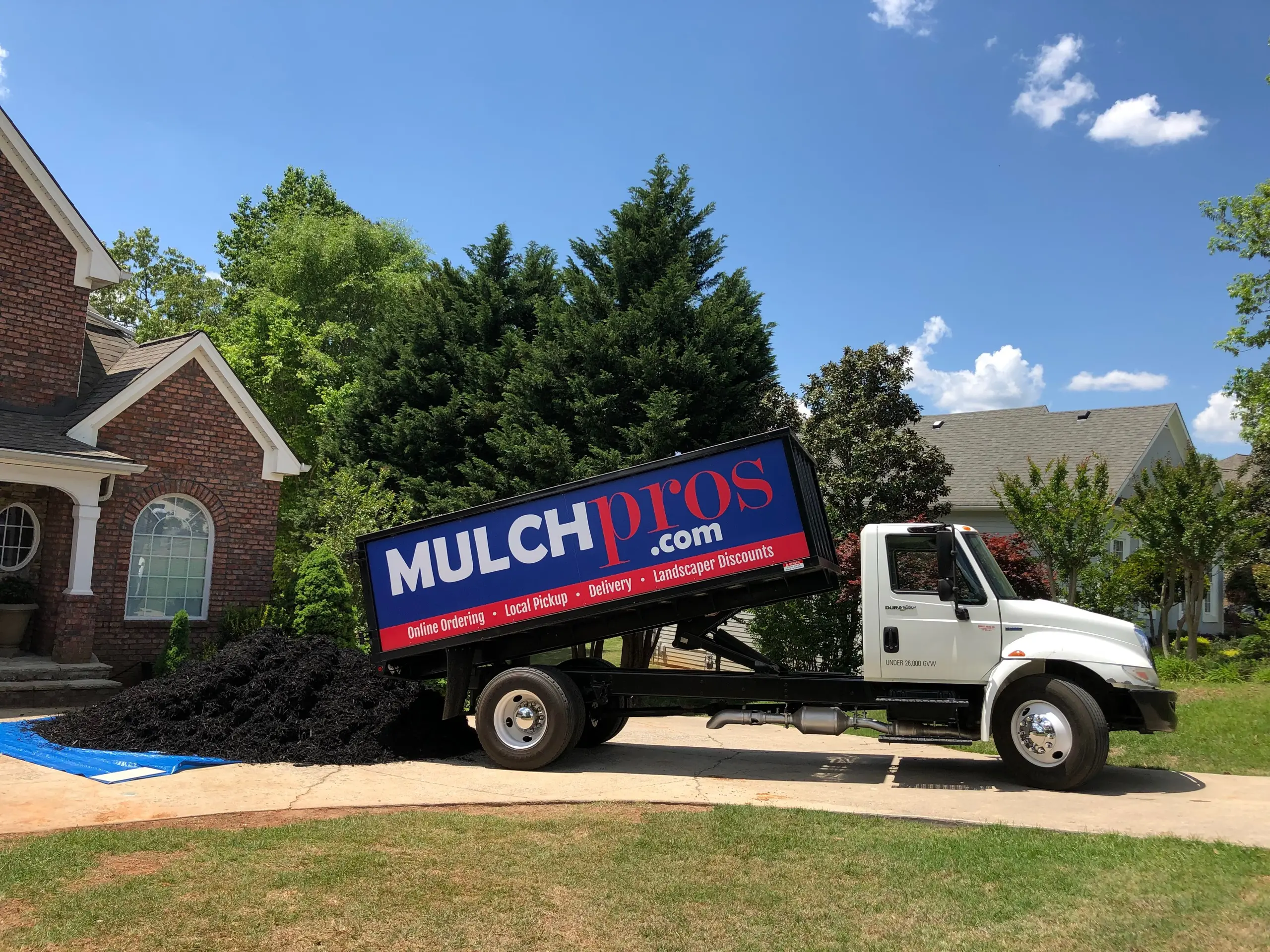Camión de volteo de MulchPros entregando mantillo negro en la entrada de una casa de ladrillo