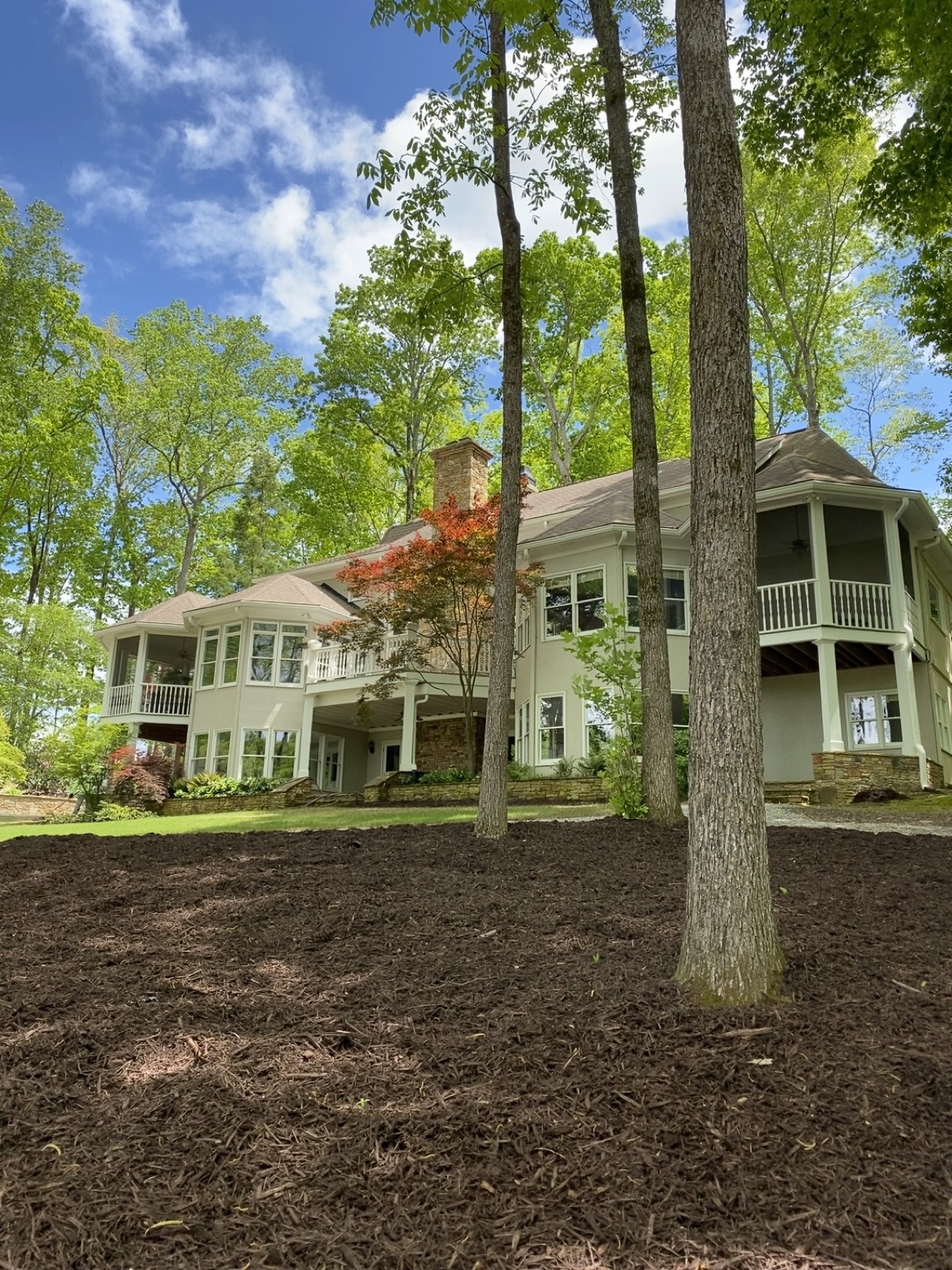Fresh brown mulch beds wrapping mature trees in front of a large white home.