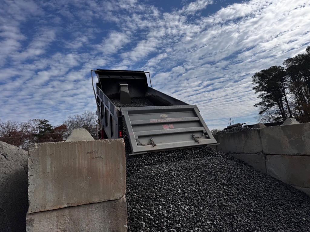 Gravel pouring from a dump trailer into a concrete block bin.