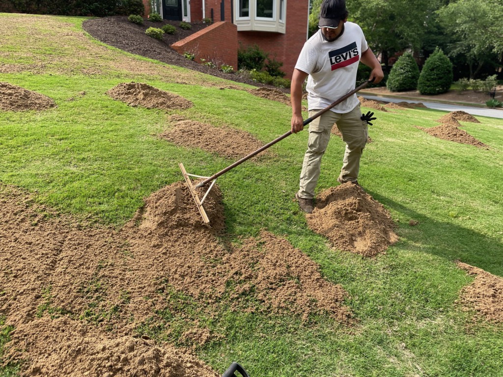 Topdressing piles being raked across a lawn at a brick home.